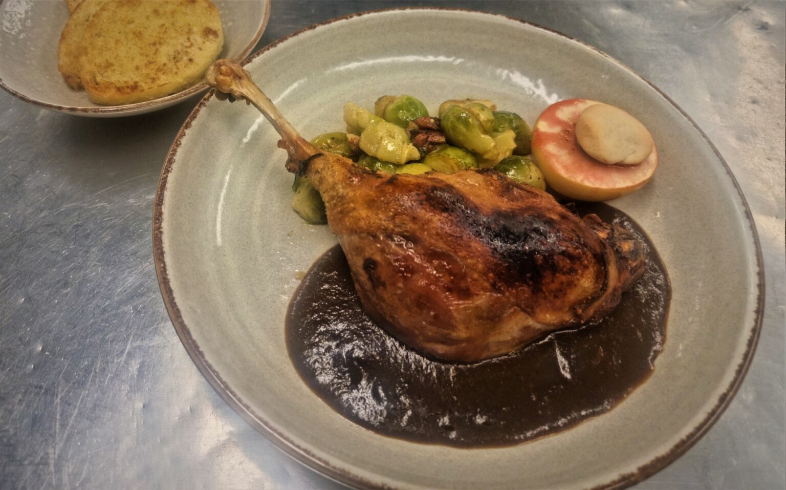 Gänsekeule angerichtet mit Sauce, Rosenkohl und Bratapfel auf einem Teller