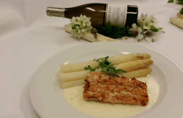 Spargel mit Fisch auf einem Teller angerichtet mit einer liegenden Flasche Weißwein